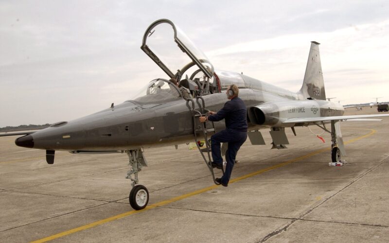 t38 talon cropped 3x2 US Air Force fighter jet on a tarmac with the cockpit canopy open and a ground crew member climbing a ladder toward the cockpit