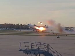 Large passenger jet lifting off the runway with a bright exhaust flame and smoky plume trailing behind at sunset