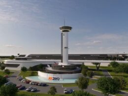 Rendering of Jet Zero facility with a tall controltower structure and circular base surrounded by a curved white building and parking lot with cars and trees