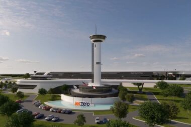 Rendering of Jet Zero facility with a tall controltower structure and circular base surrounded by a curved white building and parking lot with cars and trees