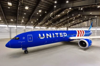 United Airlines jet painted blue parked inside a spacious maintenance hangar with its nose to the left and a visible engine on the right