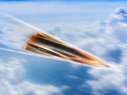 Orange and black jet like aircraft speeding to the right through a blue sky with wispy clouds motion blur