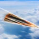 Orange and black jet like aircraft speeding to the right through a blue sky with wispy clouds motion blur