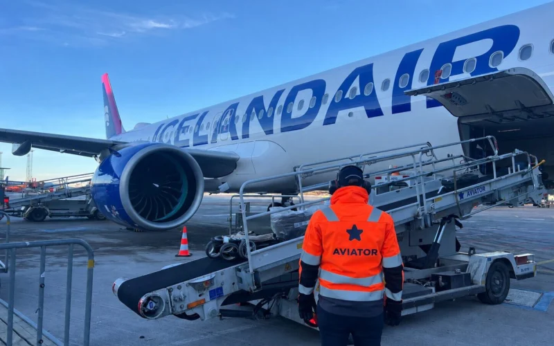 Ground crew member in a bright orange vest stands beside an Icelandair jet on the tarmac with loading stairs at the door and a large engine visible in the wing area
