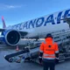Ground crew member in a bright orange vest stands beside an Icelandair jet on the tarmac with loading stairs at the door and a large engine visible in the wing area