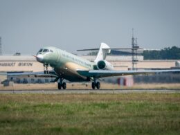 Green private jet taxis on a runway at an airfield with a Dassault Aviation hangar in the background