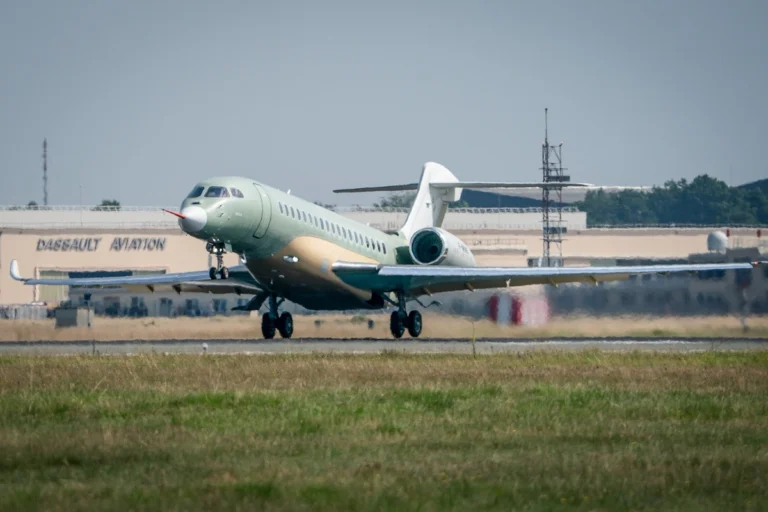 Green private jet taxis on a runway at an airfield with a Dassault Aviation hangar in the background