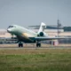 Green private jet taxis on a runway at an airfield with a Dassault Aviation hangar in the background