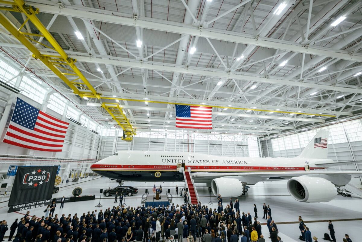 HLOC6xyXAAAp5Dc Inside a large hangar the presidential Air Force One sits on the floor beneath overhead cranes and American flags with a crowd gathered for a ceremony