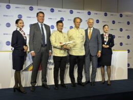 Six people on a stage at an aviation event a man holds a model airplane backdrop shows oneworld logos