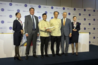 Six people on a stage at an aviation event a man holds a model airplane backdrop shows oneworld logos