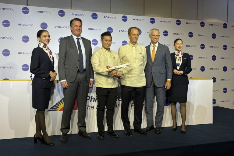 Six people on a stage at an aviation event a man holds a model airplane backdrop shows oneworld logos