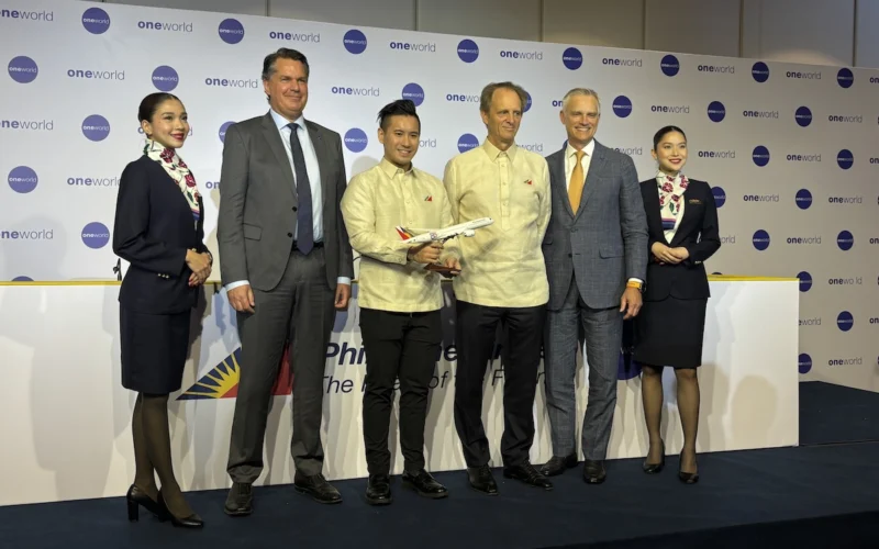 Six people on a stage at an aviation event a man holds a model airplane backdrop shows oneworld logos