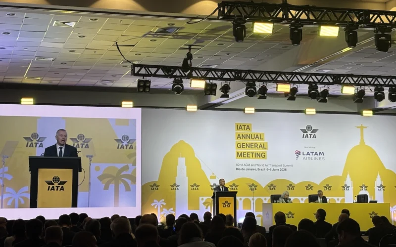 Speaker at a podium on stage during IATA Annual General Meeting with a yellow backdrop and IATA logos visible audience in foreground