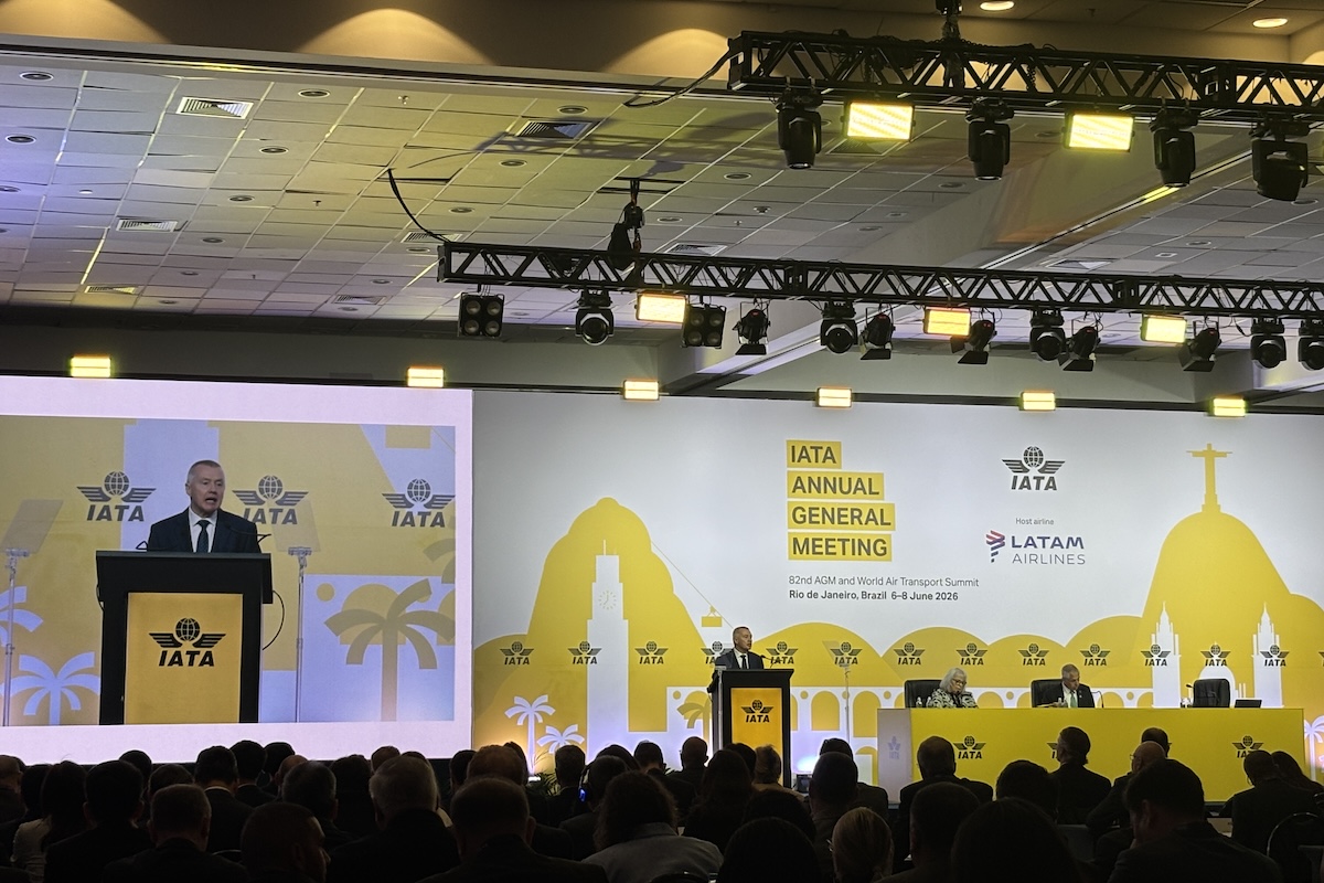 Speaker at a podium on stage during IATA Annual General Meeting with a yellow backdrop and IATA logos visible audience in foreground