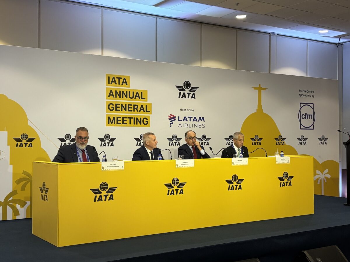 IMG 5494 Panel of suited officials at a bright yellow dais during the IATA Annual General Meeting with IATA logos on the backdrop and a sponsor display nearby