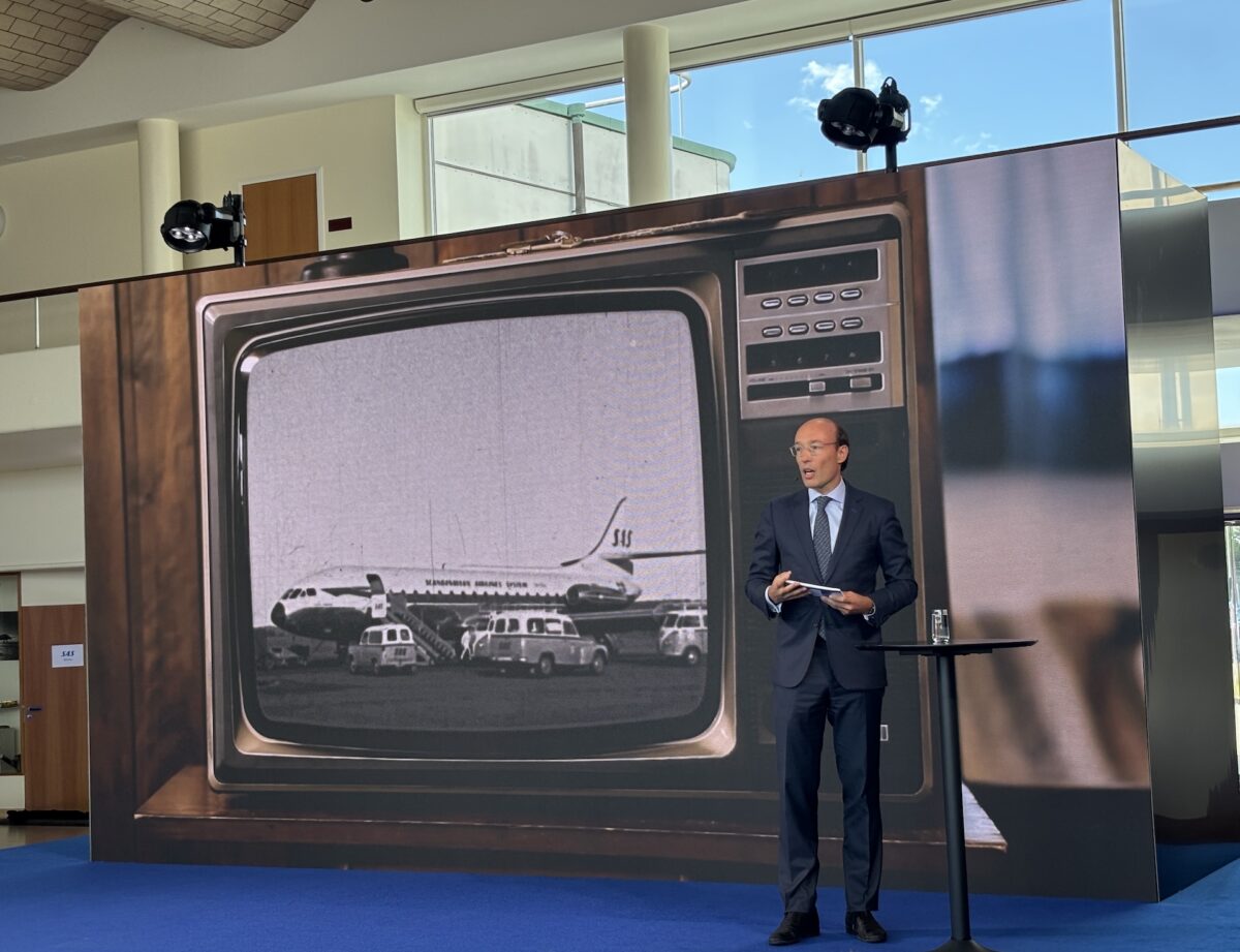 IMG 7172 Professional man in a navy suit giving a presentation on a stage with a large vintage television backdrop and blue carpet