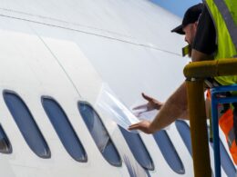 Ground crew member in a highvisibility vest applies a sheet to the windows of a white airplane on a mobile platform