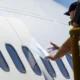 Ground crew member in a highvisibility vest applies a sheet to the windows of a white airplane on a mobile platform