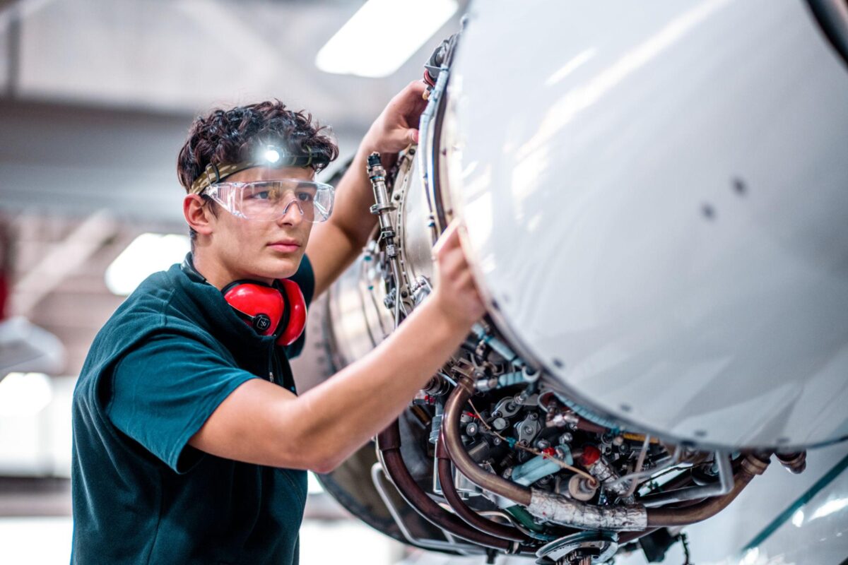 May 2nd Edition Article 3 Technician wearing safety goggles and ear protection inspects an aircraft engines exposed components from the side