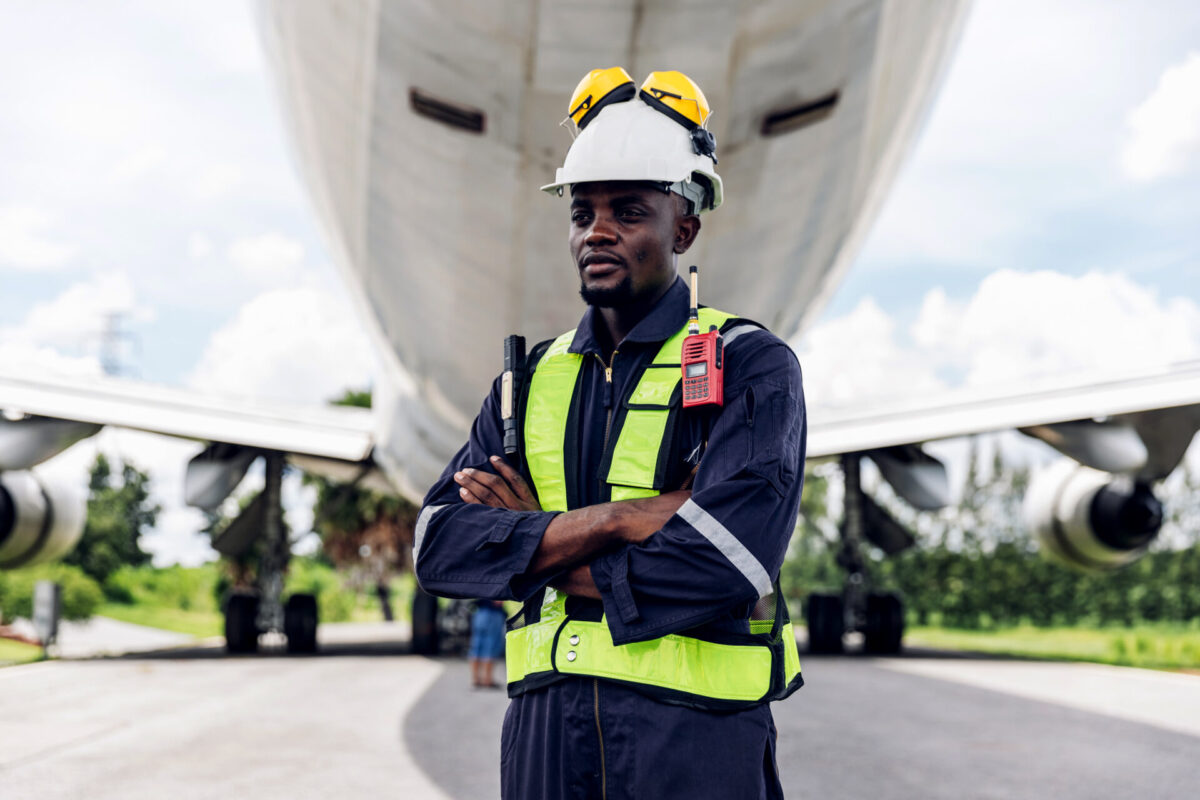 Aircraft workers checking airplane Ground personnel at the airp Ground crew worker in high visibility vest and white helmet with radio standing with arms crossed in front of a large airplane on the tarmac