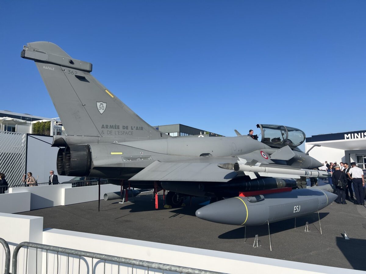 Mockup of the Rafale F5 with the Thales ESJ jamming pod at Paris Air Show 2025 Side view of a French Rafale fighter jet on display with weapons spectators behind barriers under a clear blue sky