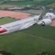 Commercial airliner in flight over green and brown fields with American Airlines livery visible on the fuselage and tailfin