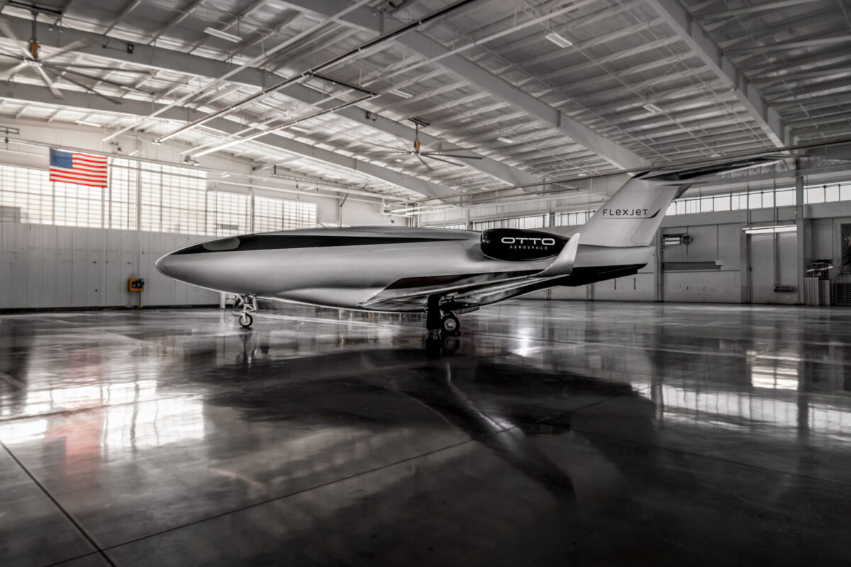 Otto Hangar Edit USA Flag Only 1 Inside a spacious hangar a sleek white and black Otto Aerospace aircraft with Flexjet branding sits on the polished floor with an American flag visible on the wall overhead