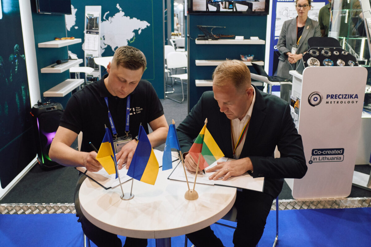 RSI Europe co founder and CEO Tomas Milašauskas and Yaroslav Tkachuk director of The Fourth Law Two men signing documents at a round table during a trade show with small national flags in front of them