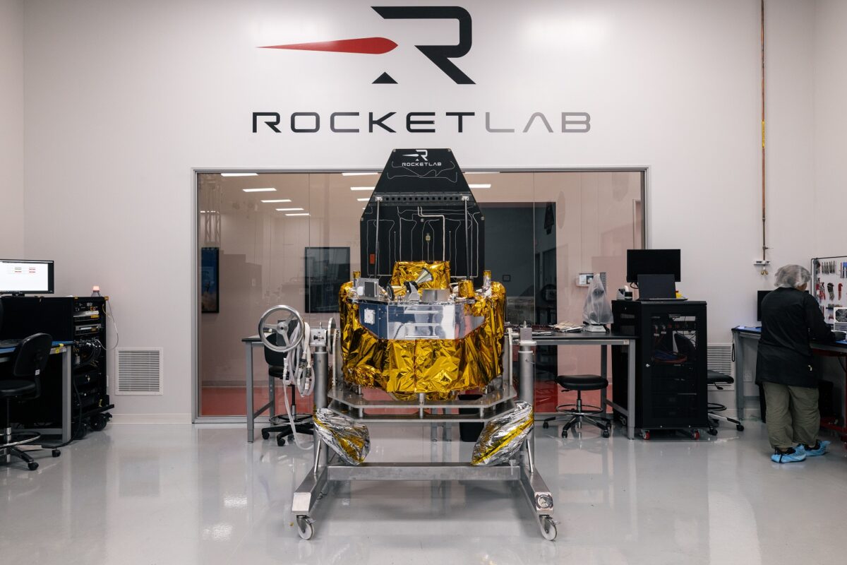 A clean lab with a gold wrapped spacecraft component on a wheeled cradle at center