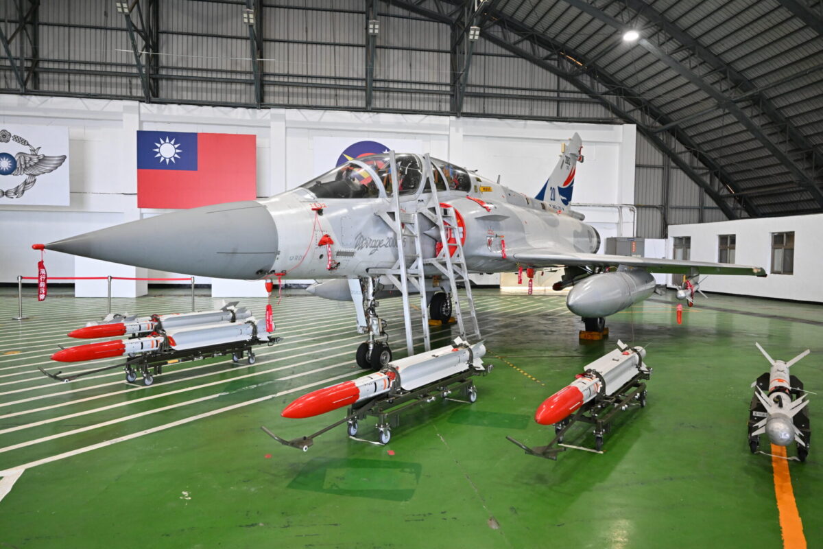 Taiwan Dassault Mirage 2000 5 Silver two seat fighter aircraft inside a hangar surrounded by red labeled missiles on wheeled racks and maintenance equipment Taiwan flag on the wall behind it