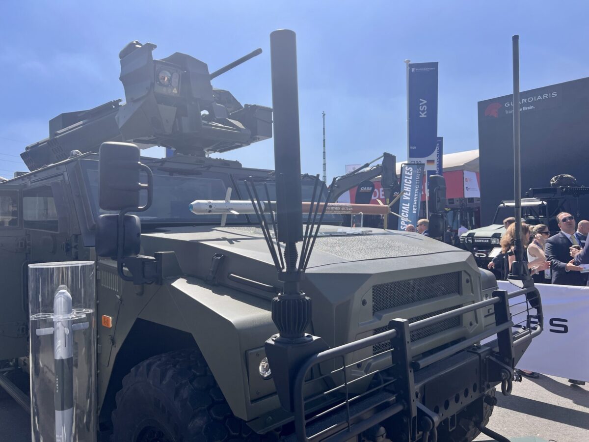 Thales Eclipse electronic warfare jammer antenna mounted at the front of the vehicle Armored military vehicle with a mounted turret on display at a sunny outdoor expo with visitors and banners in the background
