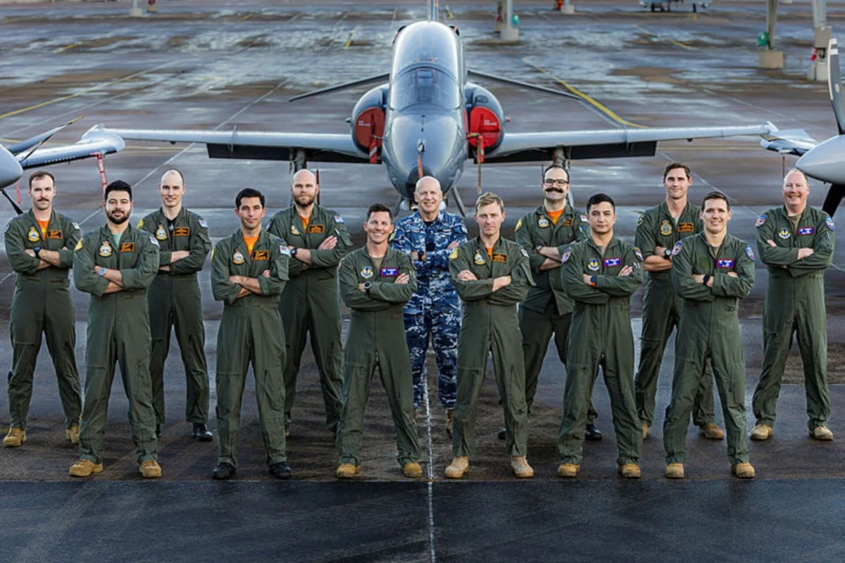RAAF hosts US Test Pilot School in rare exchange visit Group of pilots in green flight suits posing with arms crossed in front of a jet on a taxiway runway