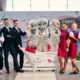 Group of staff and performers pose around a white bathtub with cocktail drinks at a promo event some wearing silver mirrored bunny heads and others in red dresses and black suits backdrop shows sponsors