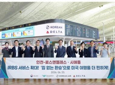 Group of professionals at an airport holding a large banner with Korean Air and Delta logos visible date 20260623 and flight information boards in the background