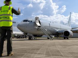 Ground crew member in a neon safety vest gives a thumbs up beside a parked jet with portable stairs