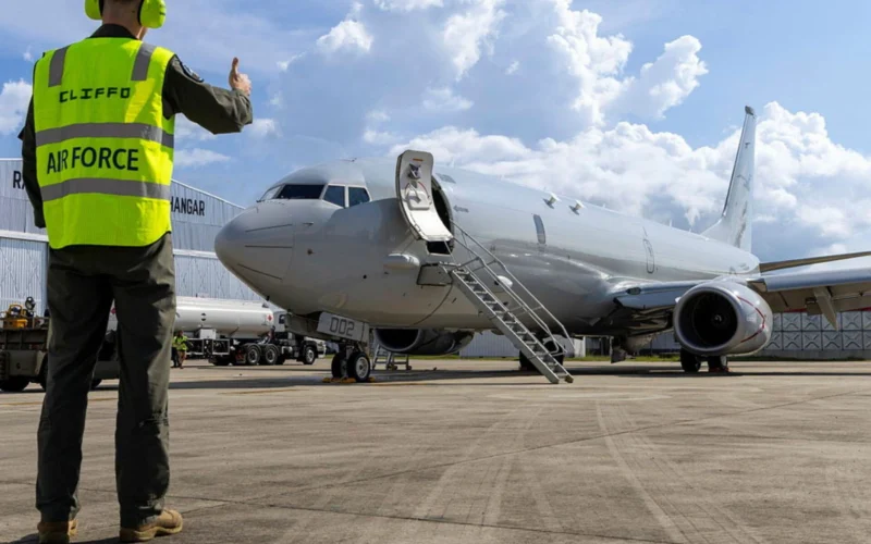Ground crew member in a neon safety vest gives a thumbs up beside a parked jet with portable stairs
