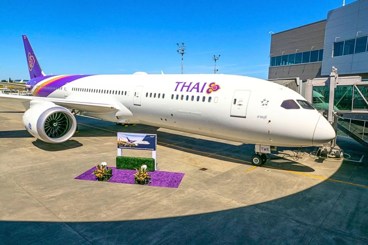 Thai Airways aircraft docked at a gate with a purple tail and logo boarding bridge on the right and a purple floral display in the foreground
