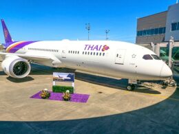 Thai Airways aircraft docked at a gate with a purple tail and logo boarding bridge on the right and a purple floral display in the foreground
