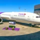 Thai Airways aircraft docked at a gate with a purple tail and logo boarding bridge on the right and a purple floral display in the foreground