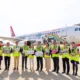 Group of airline staff in neon vests posing in front of a panda themed Hong Kong Airlines plane on the tarmac