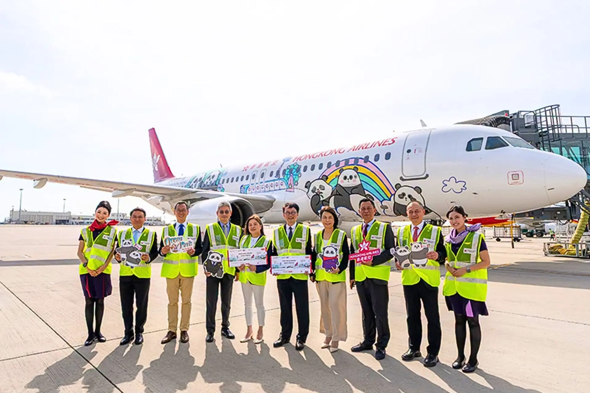 Group of airline staff in neon vests posing in front of a panda themed Hong Kong Airlines plane on the tarmac