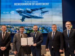Five men in suits pose with a signed memorandum of agreement in front of a large blue backdrop displaying a cargo aircraft and a city skyline