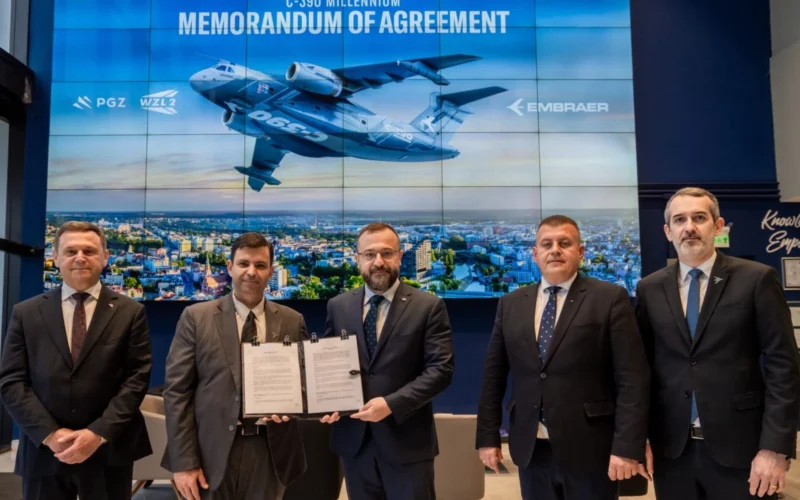 Five men in suits pose with a signed memorandum of agreement in front of a large blue backdrop displaying a cargo aircraft and a city skyline