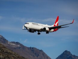 Qantas passenger jet in flight over rugged mountain landscape with a clear blue sky tail logo visible