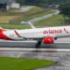 Avianca passenger jet taxiing on a wet runway red tail and logo visible