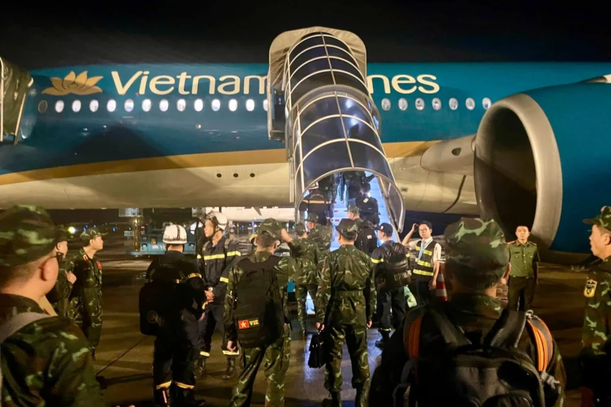 Nighttime scene at an airport a Vietnam Airlines plane with a glass boarding stair deployed and soldiers on the tarmac nearby