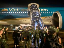 Nighttime scene at an airport a Vietnam Airlines plane with a glass boarding stair deployed and soldiers on the tarmac nearby