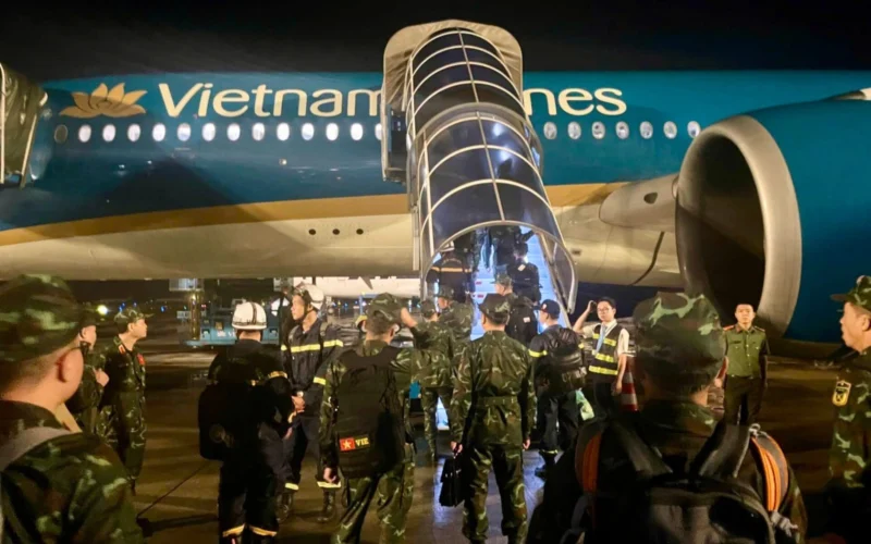 Nighttime scene at an airport a Vietnam Airlines plane with a glass boarding stair deployed and soldiers on the tarmac nearby