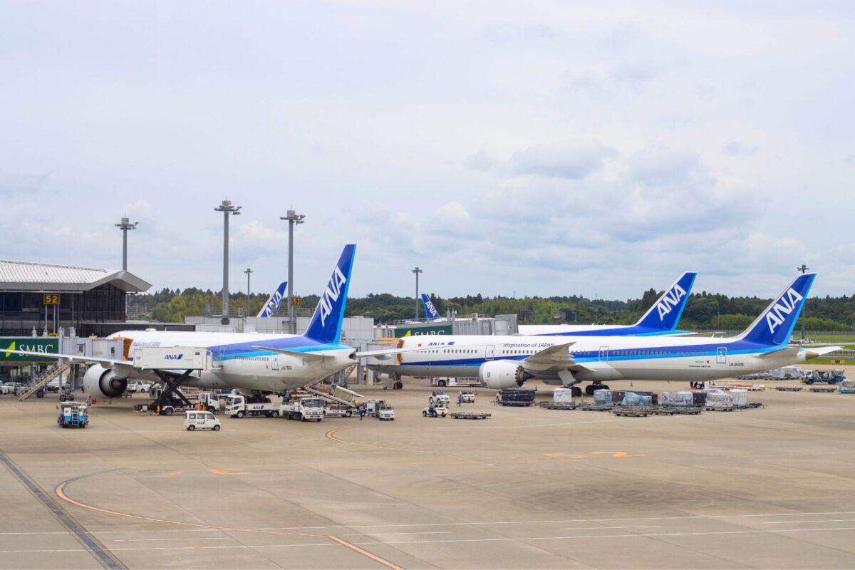 ANA Holdings invests in Phoxter to automate cargo ops Airport tarmac with several ANA airplanes docked at gates boarding bridges and ground crew working under a cloudy sky